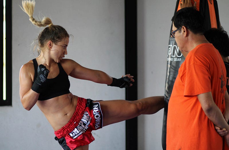 Female Thai boxing student landing a roundhouse kick on the heavy bag